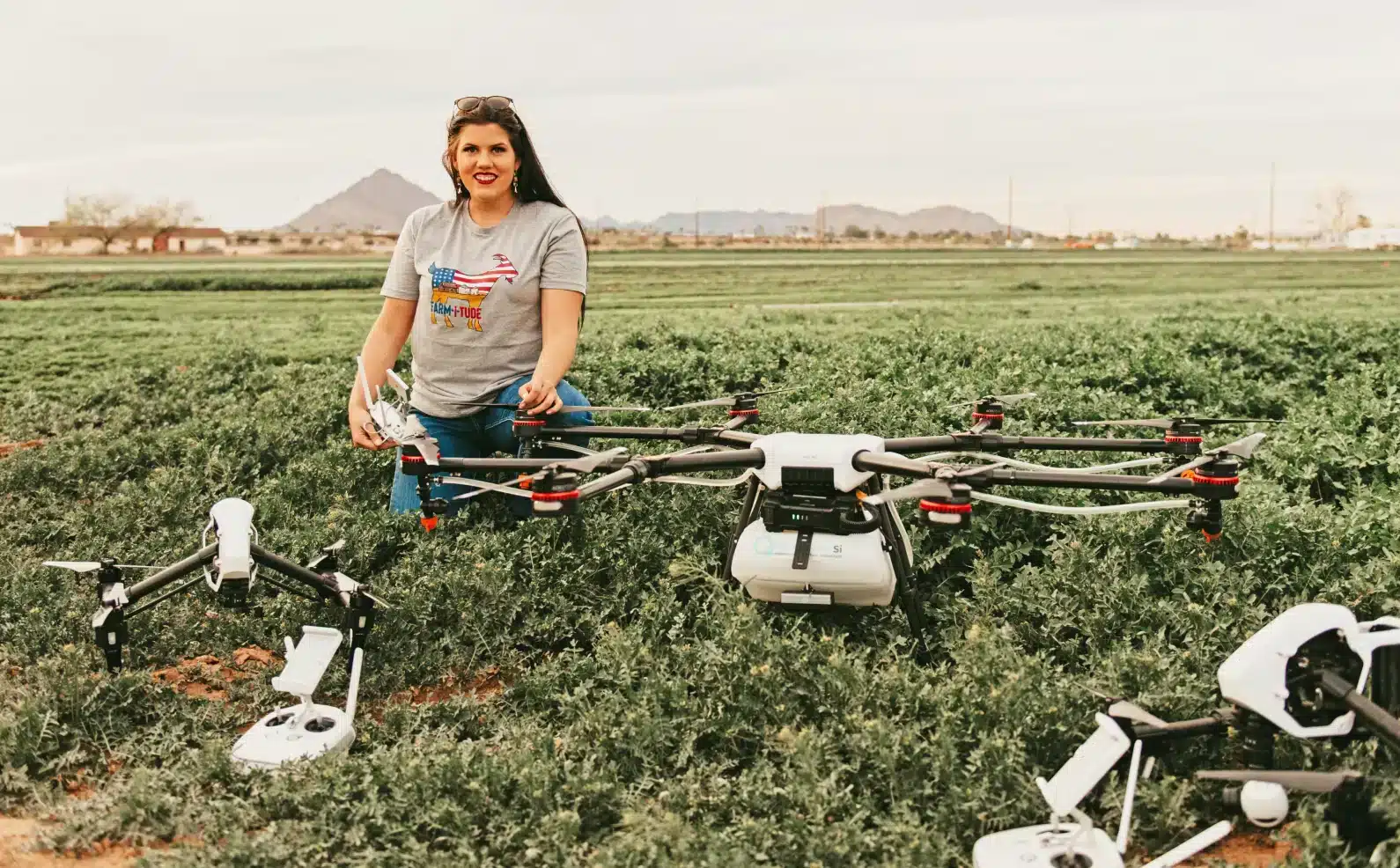 Farm-i-tude drone operator kneeling beside an agricultural spraying drone in a green field