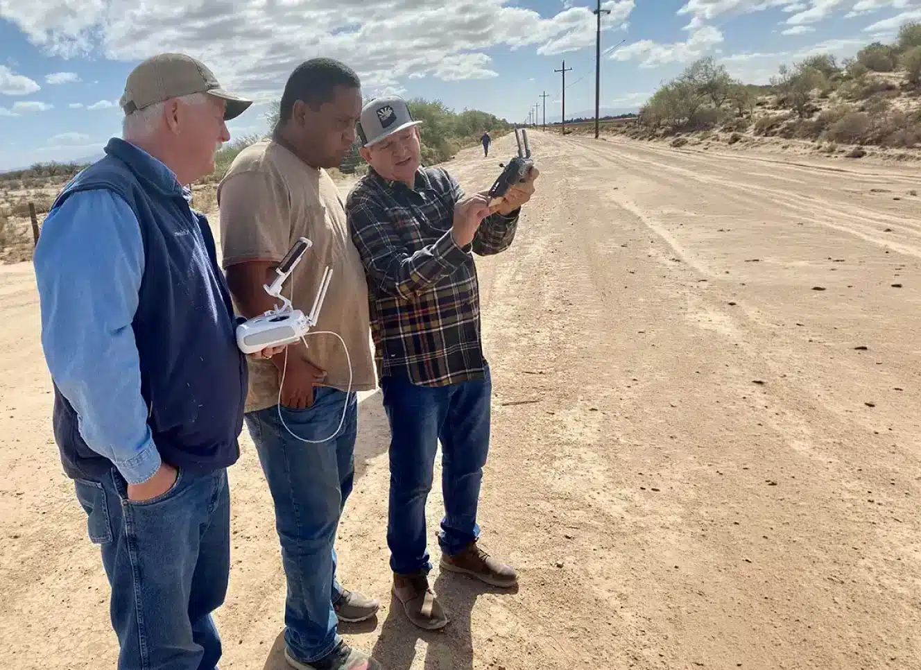 Farm-i-tude support team members training with a drone remote controller in a rural field, representing customer support and pilot training services